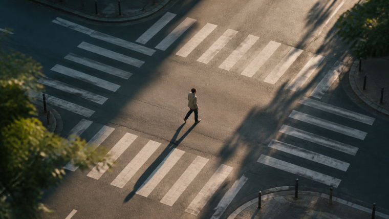 Un homme traverse seul un carrefour vide, au milieu de passages piétons, dans une lumière rasante